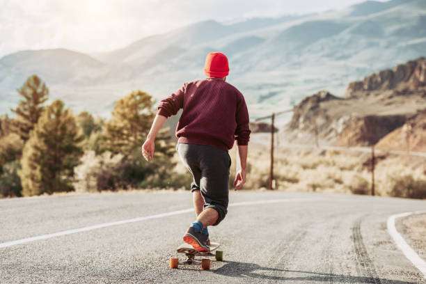 Rear view of person in red beanie riding a longboard down a winding mountain road.