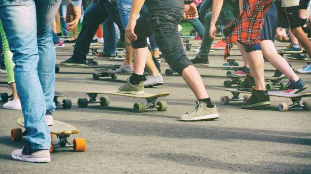 People riding various longboards on a paved surface, showing their legs.