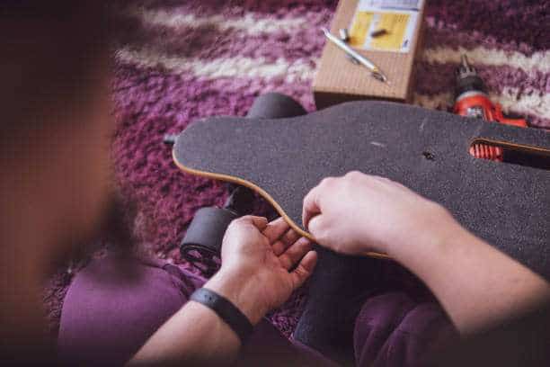 Hands applying grip tape or assembling a longboard on a fuzzy rug.