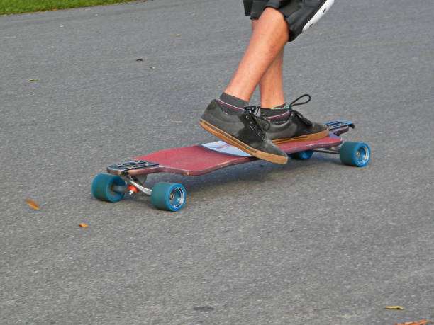 Person riding a red longboard with blue wheels on an asphalt path.