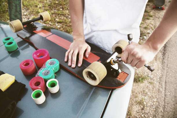 Person assembling a longboard on a car hood with colorful wheels.