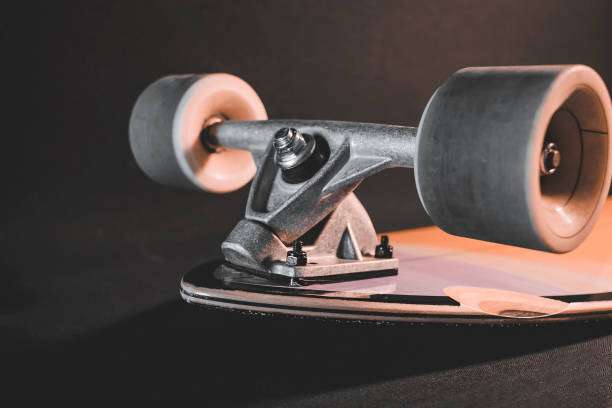 Underside view of a longboard's silver truck and large white wheels on dark background.