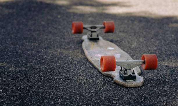 A longboard with vibrant red wheels resting on dark asphalt, ready to ride.