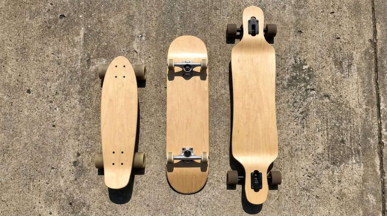 A cruiser board, longboard, and skateboard arranged by size on a concrete surface — showing the three options side by side