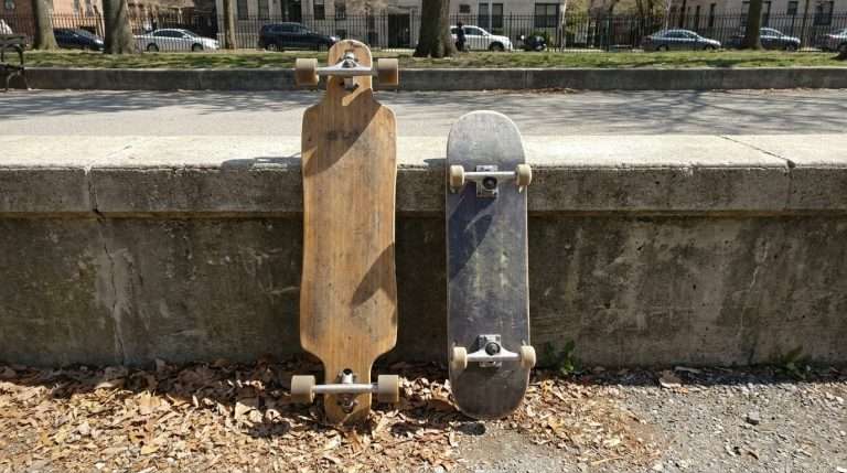 A longboard and a skateboard leaning against the same wall side by side — size and shape comparison in a real-world setting